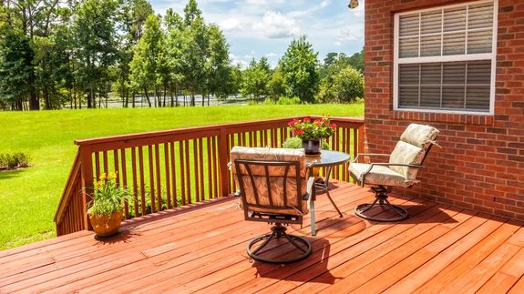 Wooden deck with patio table, chairs with cushions, and potted plants