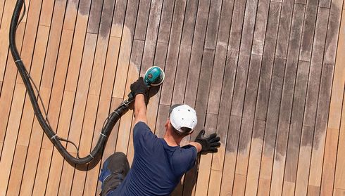 Person sanding a wooden deck with an electric sander