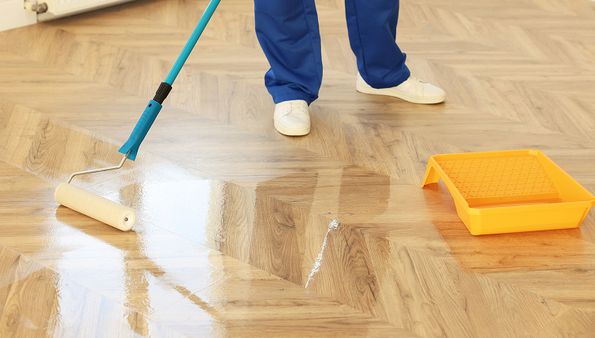 Person applying finish to hardwood floor with roller