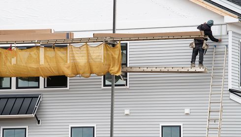 Worker installing gray vinyl siding on a house exterior using scaffolding