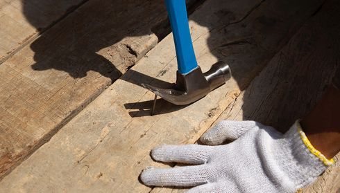 A hammer pulls a nail from a wooden plank