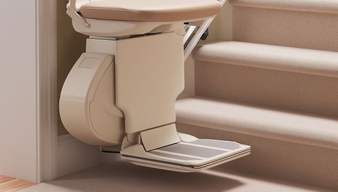 A stairlift on a carpeted staircase with a beige seat and footrest