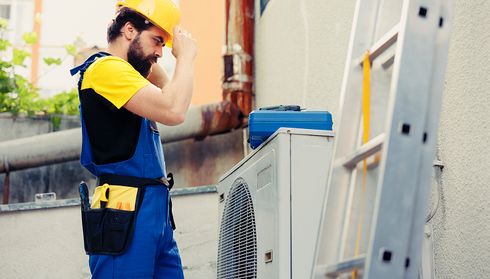 Worker adjusts equipment near an air conditioning unit