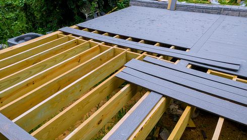 Partially constructed outdoor deck with wooden beams and partially installed gray decking boards