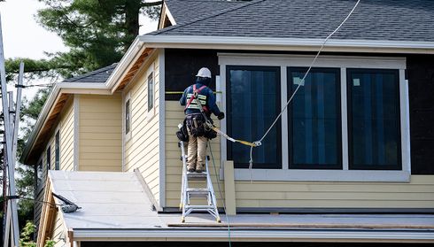 Worker on ladder installing yellow vinyl siding on a house exterior