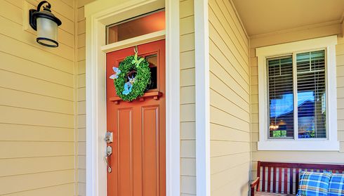Beige vinyl siding on a house porch with red front door and window