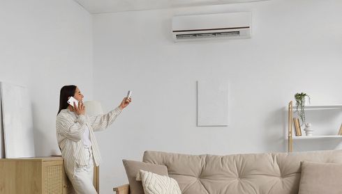 A woman adjusting the air conditioner with the remote