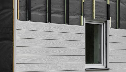Gray vinyl siding being installed on a house exterior, showing underlayment and partially exposed panels