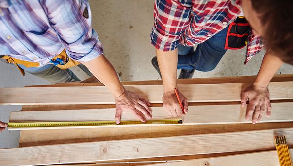 Two people measuring wooden planks