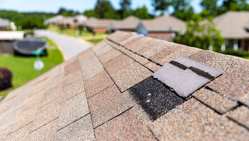 Damaged asphalt shingles with patch repair before roof replacement