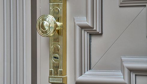 An ornate brass door handle and lock on a beige paneled door