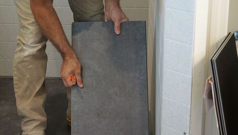 Person installing a large, rectangular dark tile on a floor