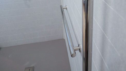 Shower area with light gray tiles, featuring a mounted metal grab bar